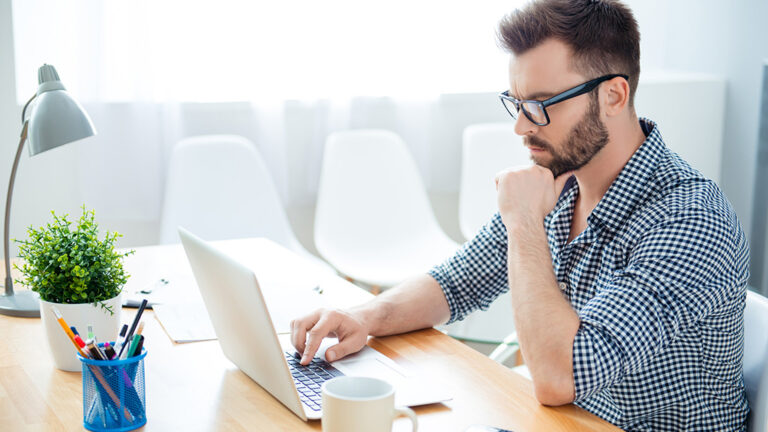 A man sits looking intently at laptop.