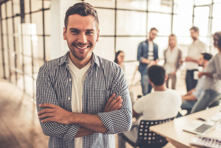 Man smiles at camera as a group of business owners behind him discuss opening a US LLC.