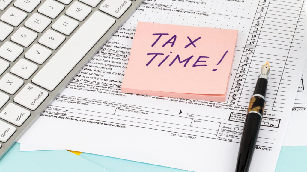 Formulario de impuestos del IRS con una nota adhesiva que dice "¡Tiempo de impuestos!" y teclado de computadora portátil.