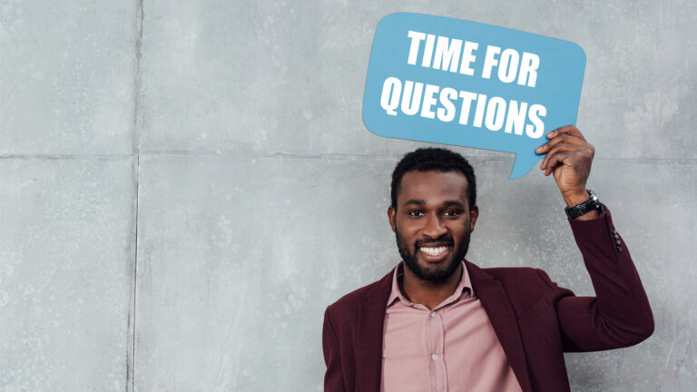 Man in business casual holding a sign with time for questions.