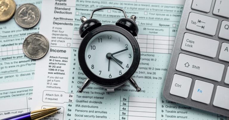 US tax deadlines with alarm clock, IRS forms, coins, and keyboard – reminder for 2025 compliance filing.